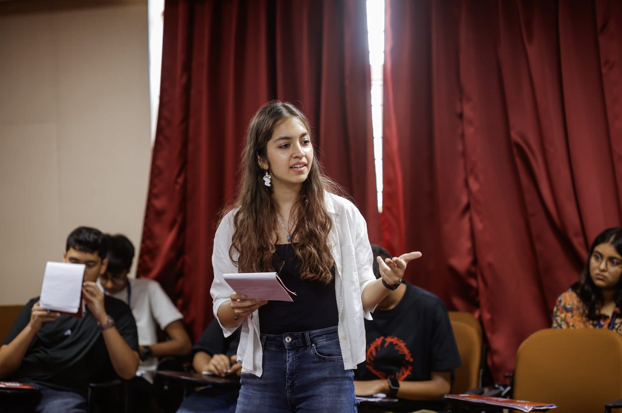 A Taivas student on her feet mid-speech, notes in hand, in front of her batch