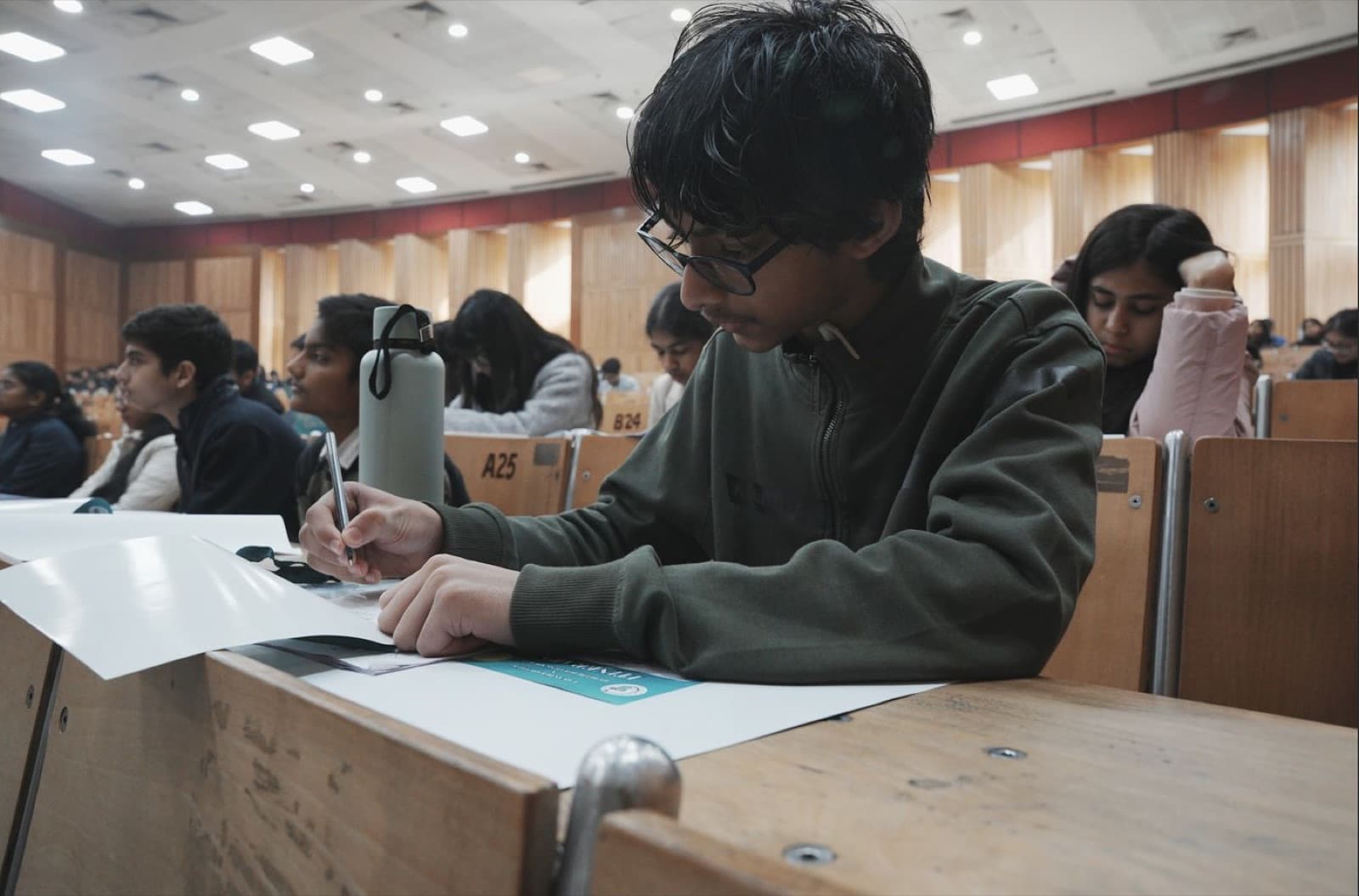 A student writing notes at a desk in a hall