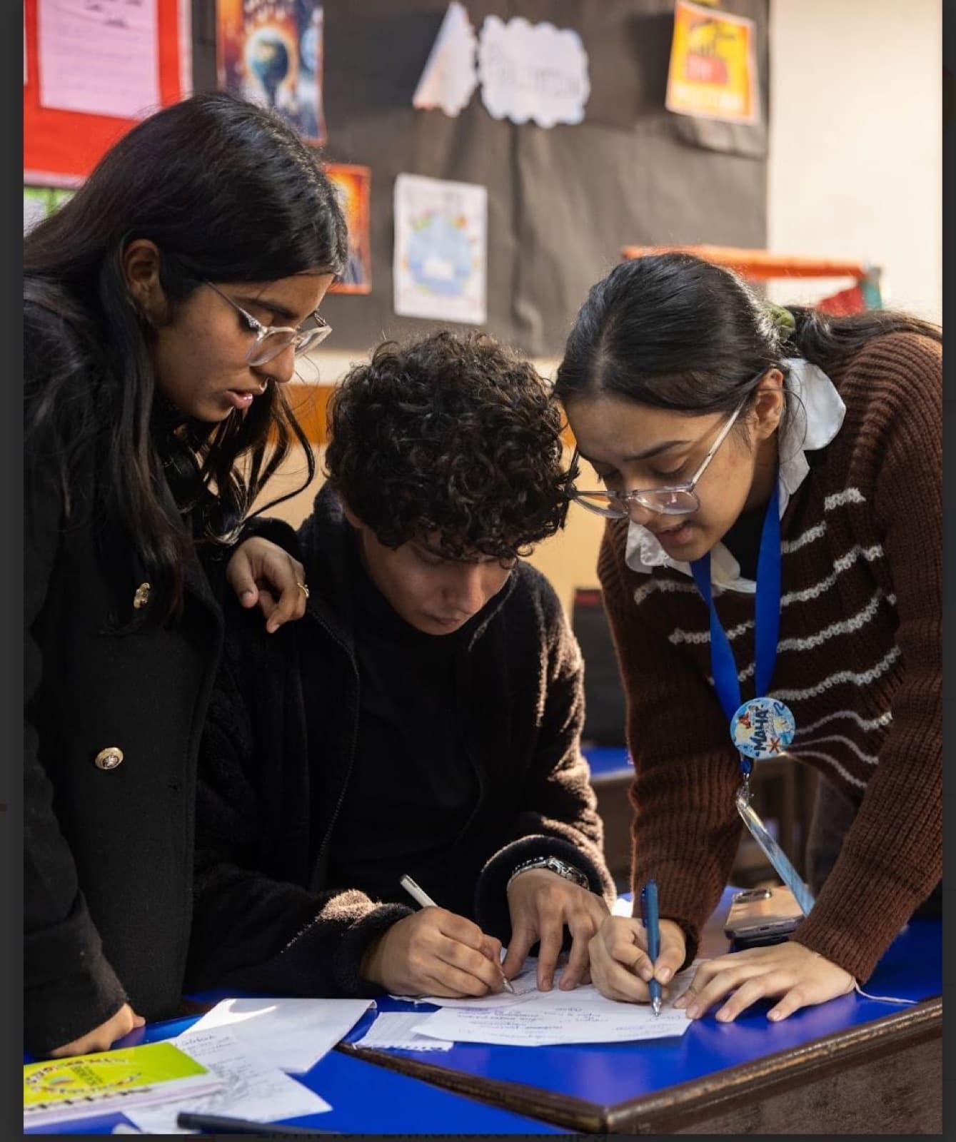 Three students leaning over one desk, working an idea out together on paper